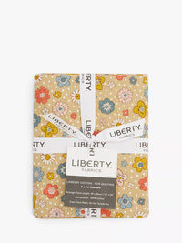A packaged quilt fabric bundle from Liberty Fabrics, featuring a floral pattern on a warm beige background with white, blue, yellow, and red flowers. The bundle is wrapped in a white paper band and a central label.